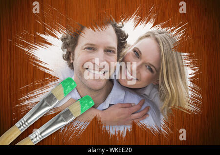 Composite image of couple smiling at camera with paintbrush dipped in green against wooden oak table Stock Photo