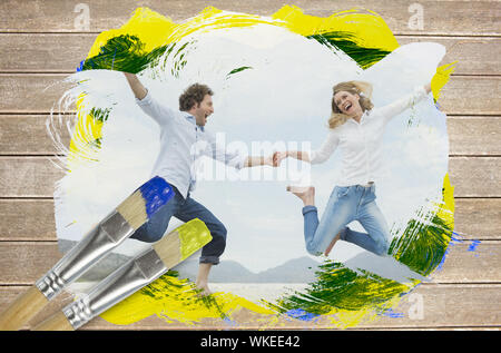 Composite image of couple jumping on the beach with paintbrush dipped in yellow against wooden surface with planks Stock Photo