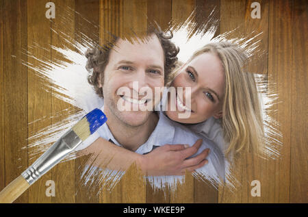 Composite image of couple smiling at camera with paintbrush dipped in blue against wooden surface with planks Stock Photo