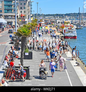 Poole Harbour view of summer season group of people seen from above walking along harbour promenade quay tour boat & marina beyond Dorset England UK Stock Photo