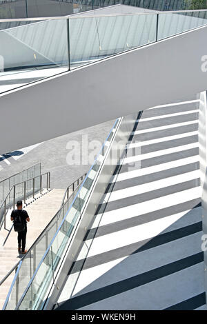 Back view of man walking alone down steps from walkways & ramps at “The Tide” a linear park of elevated walks above North Greenwich London England UK Stock Photo