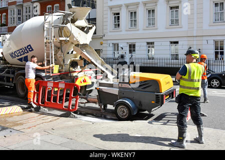 Workmen & pre mixed cement floor screed from concrete delivery truck lorry to small trailer pumping via hose to building construction site London UK Stock Photo
