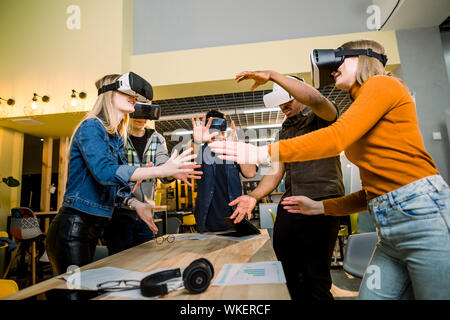 Happy young business people in casual wear watching video in vr headset, gesturing and having fun Stock Photo