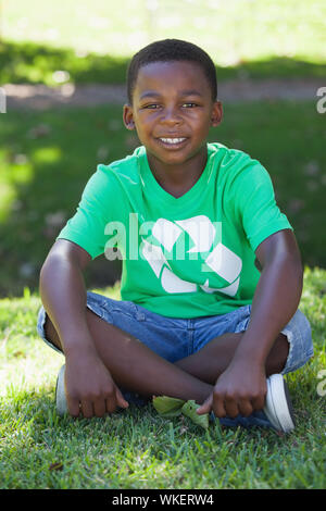 Young boy sitting on grass in recycling tshirt on a sunny day Stock Photo