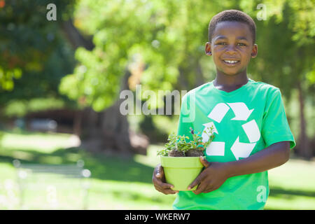Young boy in recycling tshirt holding potted plant on a sunny day Stock Photo