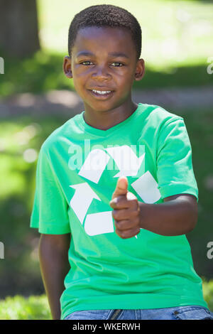 Young boy sitting on grass in recycling tshirt showing thumb up on a sunny day Stock Photo