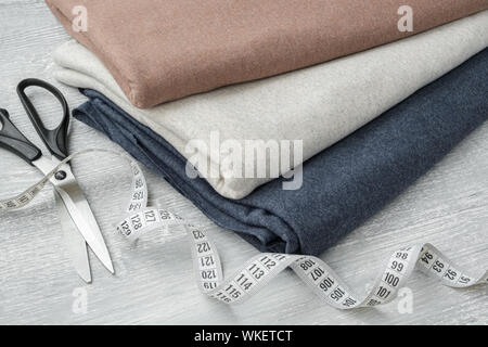Stack of knitted jersey fabrics, tailoring scissors and measuring tape on table. Stock Photo
