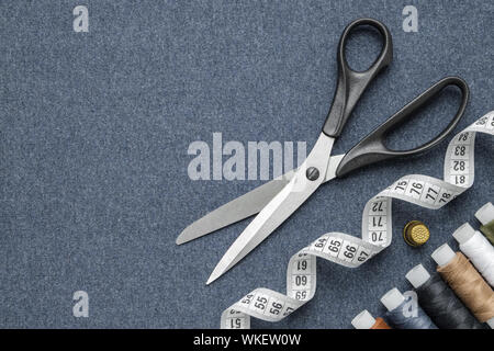 Sewing items: tailoring scissors, measuring tape, thimble, spools of multicolored threads. Sewing accessories on sewing cloth. View from above. Stock Photo