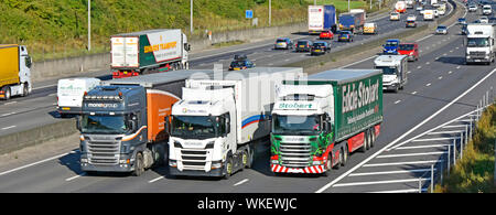 Supply chain hgv lorry truck drivers in cabs of articulated trailer vehicles overtaking in traffic lorries trucks busy four lane motorway England UK