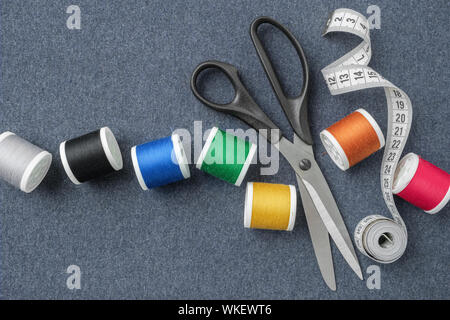 Sewing items: tailoring scissors, measuring tape, spools of multicolored threads. Sewing accessories on sewing cloth. View from above. Stock Photo
