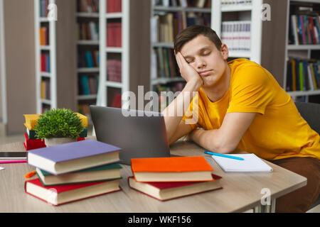 Male student sleeping at workplace in college library Stock Photo