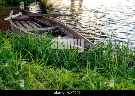 A small wooden rowing boat with a broken bottom on a calm lake near the shore. Belarus