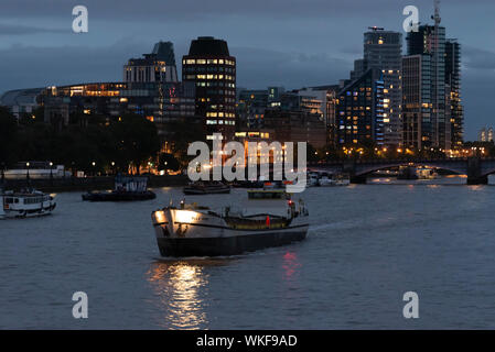 Polla Rose cargo vessel freight boat with London skyline at dusk with lights on the buildings in evening. River Thames river traffic. Night. Dark Stock Photo