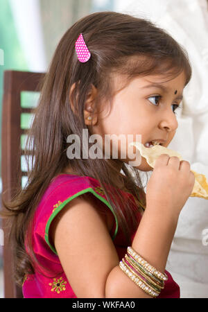 Indian family dining at home. Candid photo of Asian child self feeding snack papadum. India culture. Stock Photo