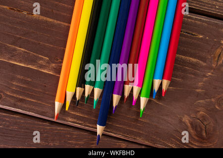 Group of twelve whole colored pencil rainbow colors flatlay on brown wood Stock Photo