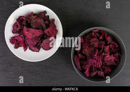 Lot of slices of dried red beetroot on white ceramic plate in gray ceramic bowl flatlay on grey stone Stock Photo