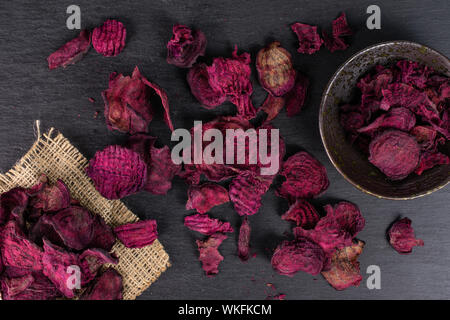Lot of slices of dried red beetroot on natural sackcloth in dark ceramic bowl flatlay on grey stone Stock Photo
