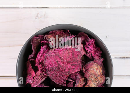 Lot of slices of dried red beetroot in gray ceramic bowl flatlay on white wood Stock Photo