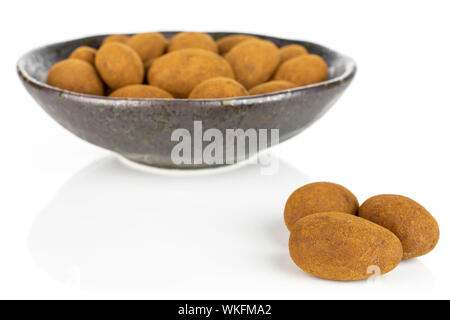 Lot of whole sweet brown chocolate cinnamon almond in dark ceramic bowl isolated on white background Stock Photo