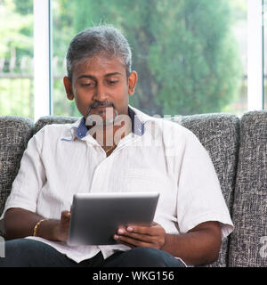 Portrait of middle aged Indian man reading on digital tablet computer at home. Stock Photo
