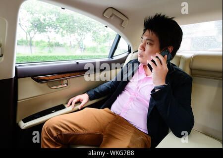Asian man talking on mobile phone and looking through documents while sitting in car Stock Photo