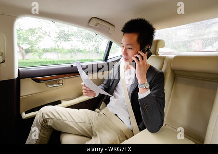Young man talking on mobile phone and looking through documents while sitting in car Stock Photo