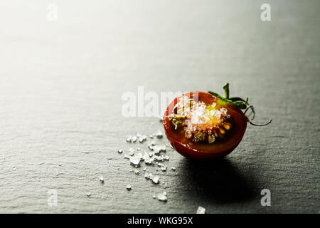 Fresh grape tomatoes with  salt for use as cooking ingredients with a halved tomato in the foreground with copyspace Stock Photo