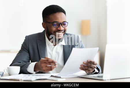 Cheerful black businessman checking reports and making notes Stock Photo
