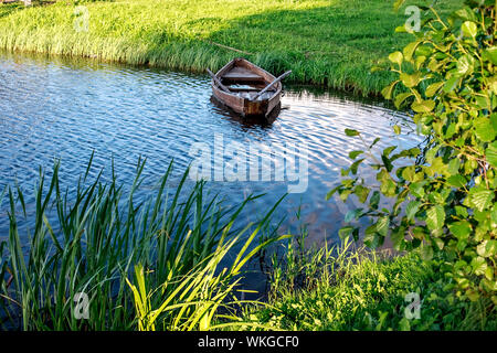 A small wooden rowing boat with a broken bottom on a calm lake near the shore. Belarus