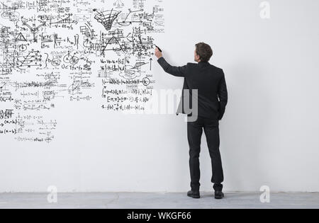 Elegant businessman rear view sketching with a black marker on a white wall. Stock Photo