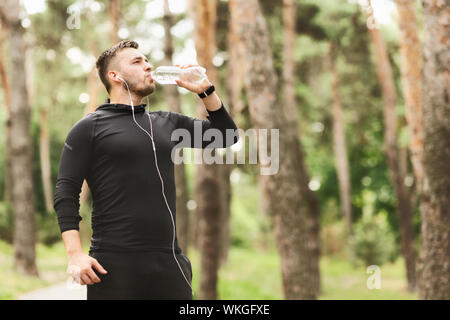 Young athletic man drinking water after training in city park Stock Photo
