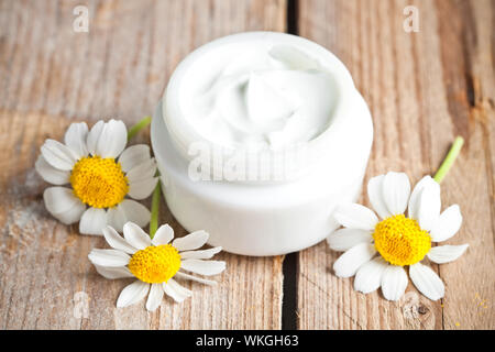 container with cream and chamomiles on wooden background Stock Photo