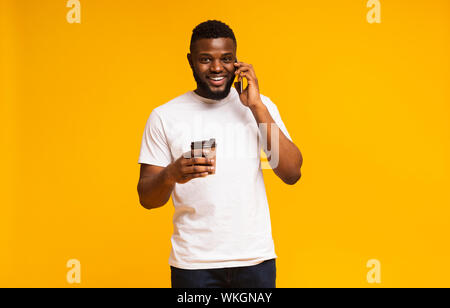 Young man holding cup of coffee and talking on smartphone Stock Photo