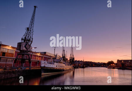 Bristol's floating harbour at sunset. In the foreground is a ship, the Balmoral. Next to it are the M-Shed cranes, disappearing down quayside. Stock Photo