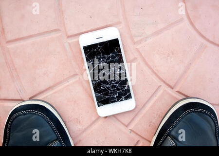 broken smartphone screen. Feet and smartphone with a broken phone screen on the tile floor. Top view broken phone Stock Photo