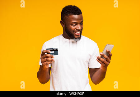 Cheerful black man using credit card and smartphone for purchasing online