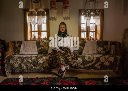 Young girl in the room with traditional furniture dressed in traditional clothes from Maramures, Romania Stock Photo