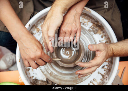 Top view at senior woman spinning clay on a wheel with a help of a teacher at pottery class Stock Photo