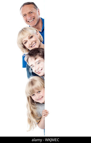 Smiling family posing from behind blank whiteboard Stock Photo