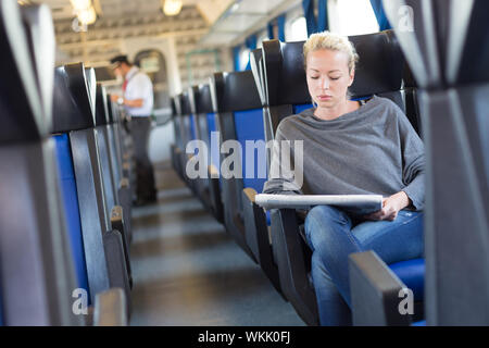 Young woman traveling by train, conductor checking  tickets in the background. Stock Photo