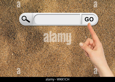 Human hand indicates the search bar in browser. Yellow sand surface on background Stock Photo