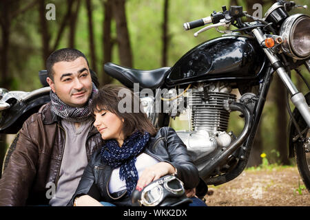 Attractive woman sleeping on shoulders of her husband, sitting near bike, relaxation after bikers tour in the forest, active and loving family concept Stock Photo