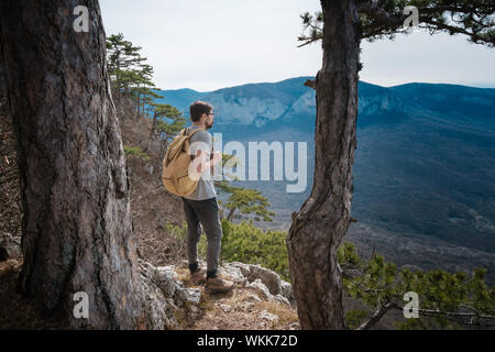 young hipster man in the spring mountains. Hipster with a backpack behind his back goes on a trip Stock Photo