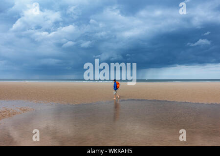 Female hiker walking on beach under a stormy sky at Saltburn on the Yorkshire coast. UK Stock Photo