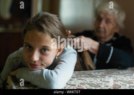 Grandma braids hair in braids to little cute girl. Stock Photo