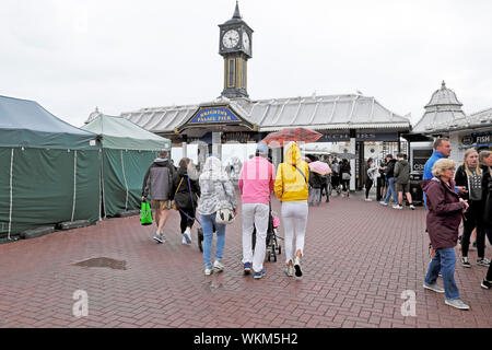 Rear back view of family walking to Brighton Pier wearing rain gear and holding umbrella in August summer East Sussex England UK  KATHY DEWITT