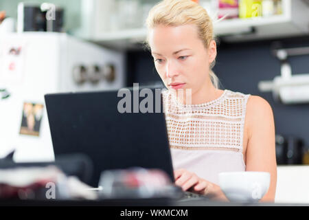 Business woman working remotly from her dining table. Home kitchen in the background. Stock Photo