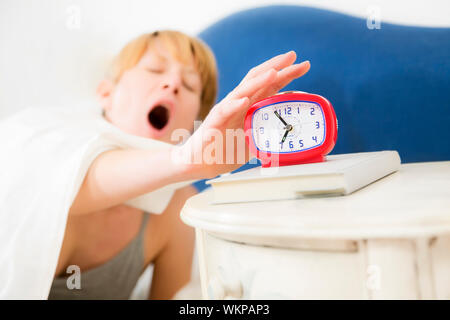 Young woman snoozing a red alarm clock Stock Photo