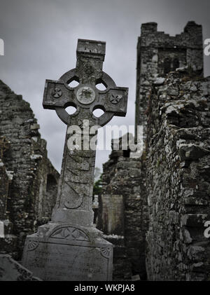 Headstone with celtic cross on a cemetery with church ruins in the background Stock Photo