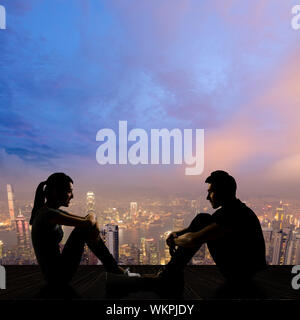 Silhouette of young couple face to face sit on ground in the city night. Stock Photo